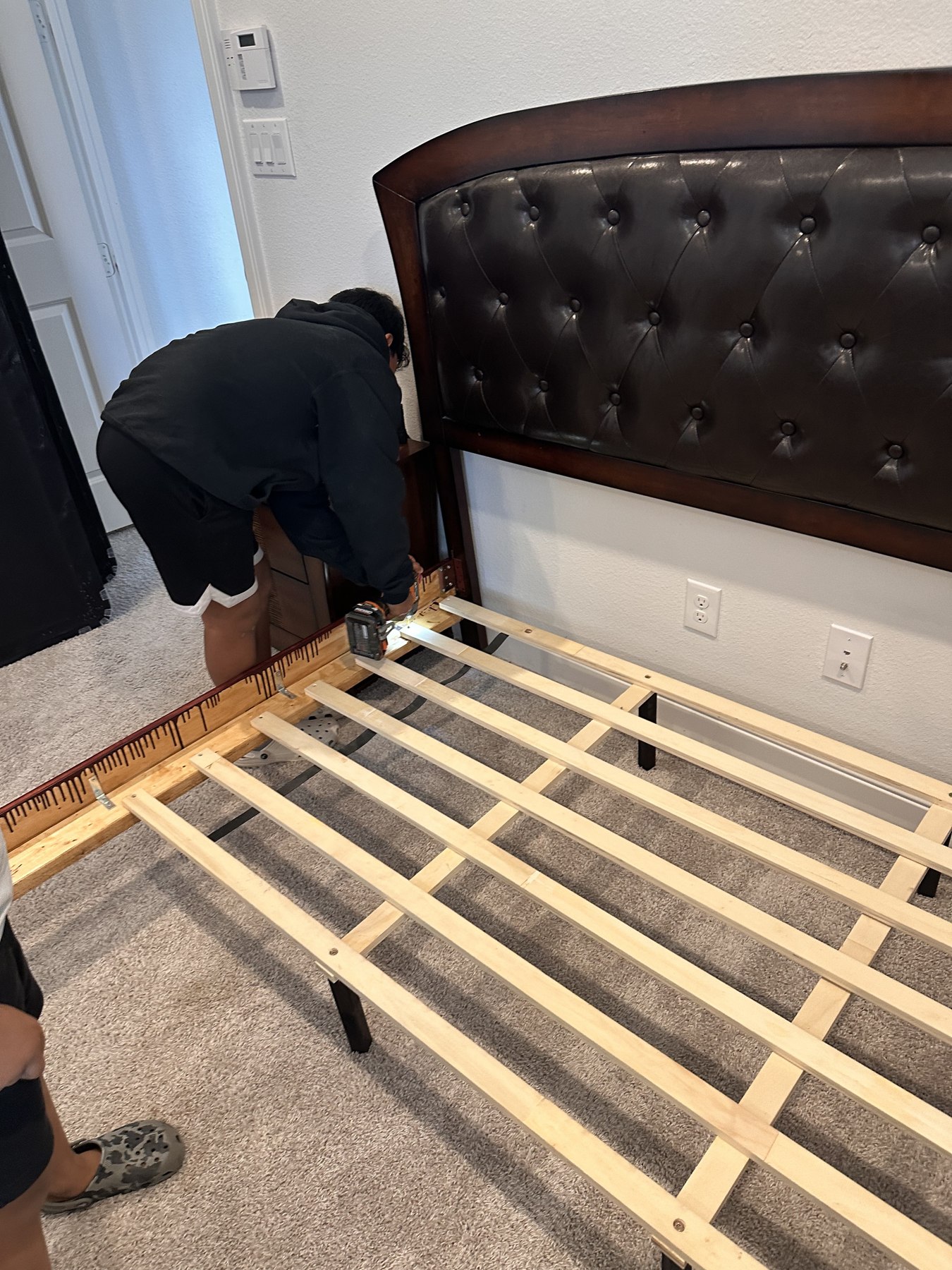 Josiah using a drill to assemble the wooden support slats of a bed